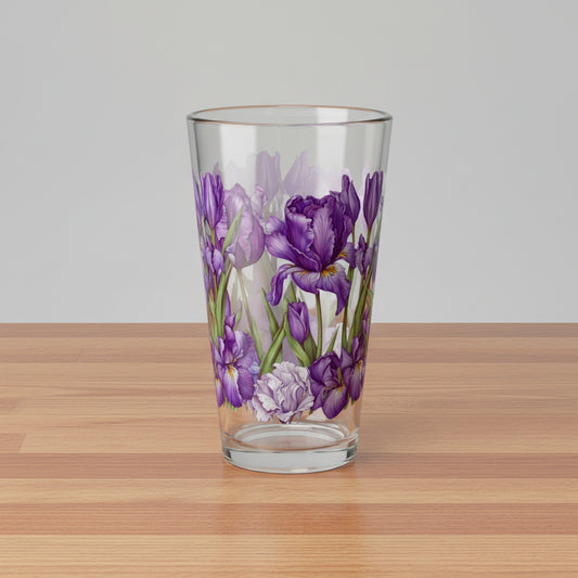 A clear glass pint glass featuring a printed design of purple irises with green stems and leaves, set against a plain white background.